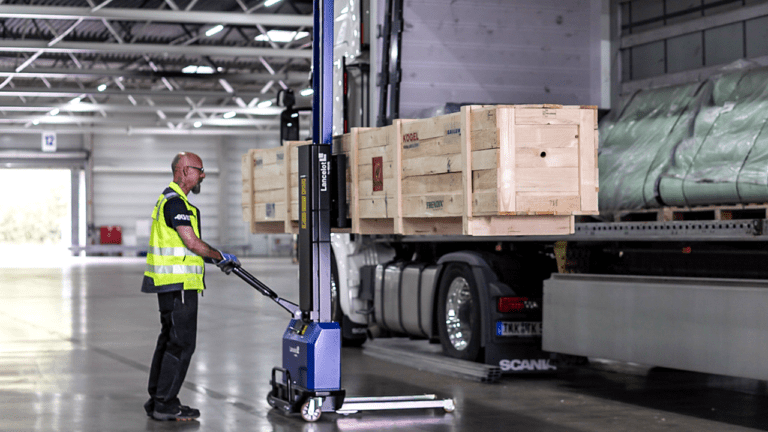 Ein LKW wird seitlich mit Langgut als Teilladung beladen, ein Lagermitarbeiter bedient dafür einen Lancelot-Hubwagen.