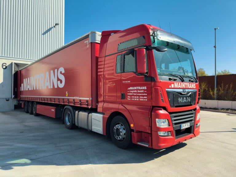 Ein roter Maintrans-LKW wird an der Laderampe eines Logistik-Lagers beladen.