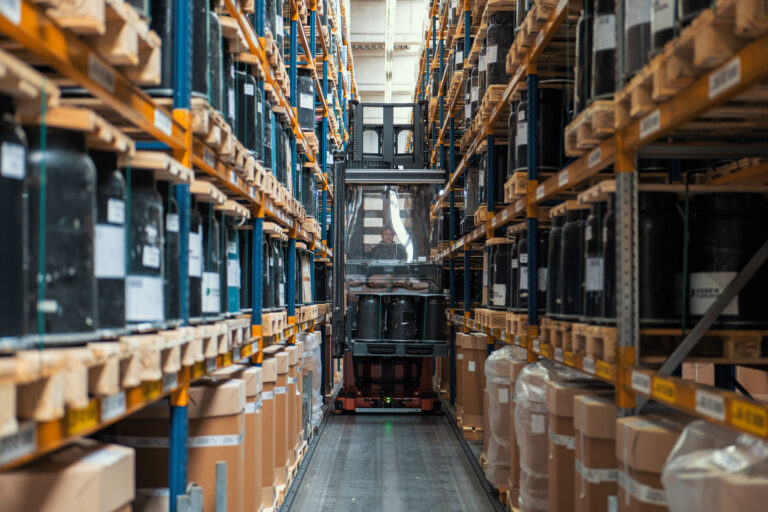 Ein Flurförderzeug fährt durch einen schmalen Gang zwischen zwei Hochregalen in einem Logistik-Lager.