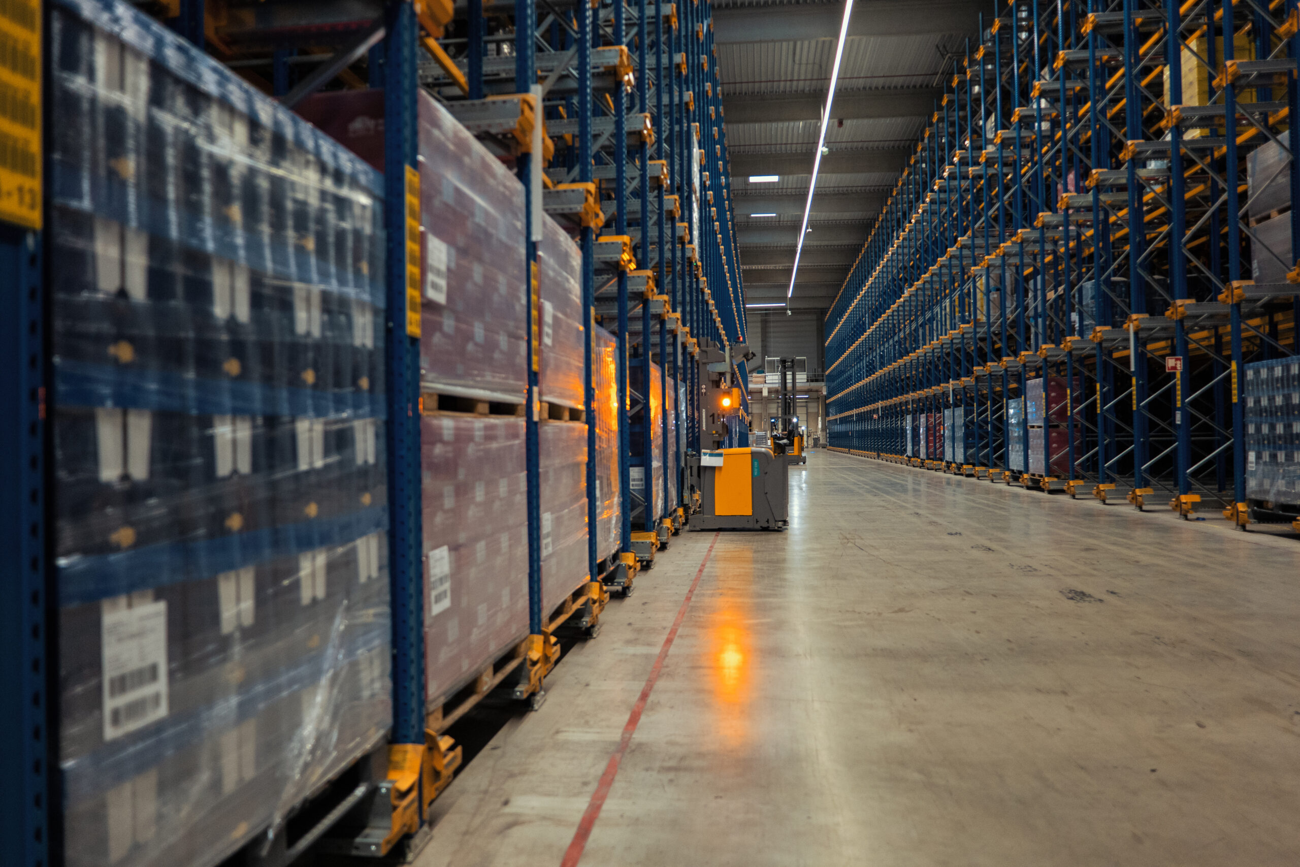 Fahrerloses Transportsystem bewegt sich zwischen zwei Regalreihen in einem automatisierten Logistik-Lager.