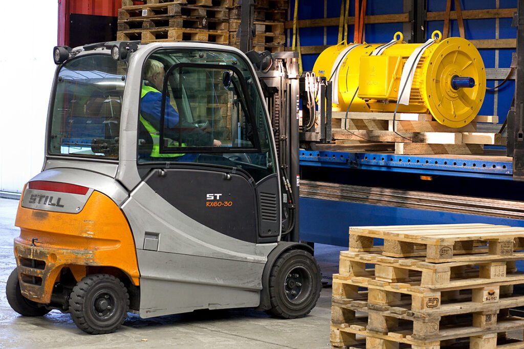 Ein Gabelstapler lädt seitlich ein Maschinenteil in einen LKW.