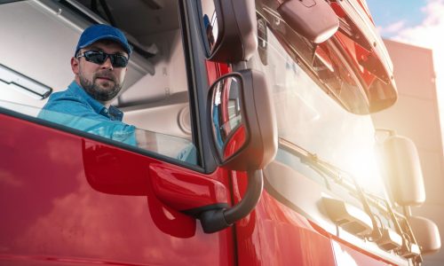 Ein LKW-Fahrer blickt aus dem Fenster der Beifahrertür seines roten LKW.